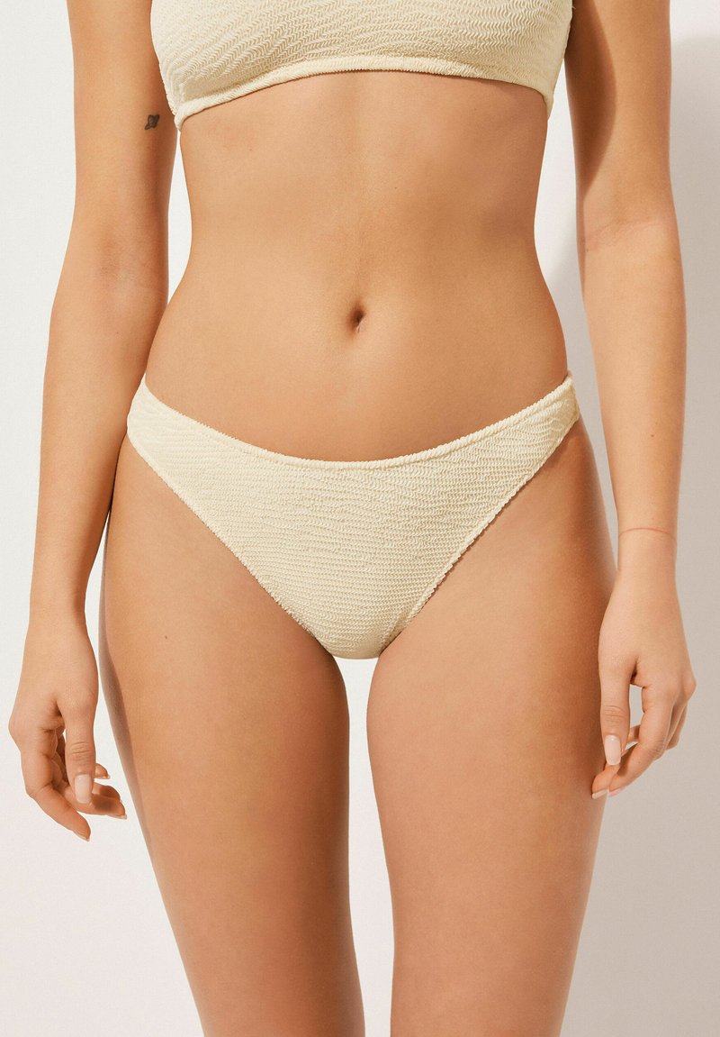 Jasno kremowe majtki bikini wykonane z teksturowanej tkaniny, z niskim stanem i bezszwowym pasem. Idealne do pływania lub na plażę.
