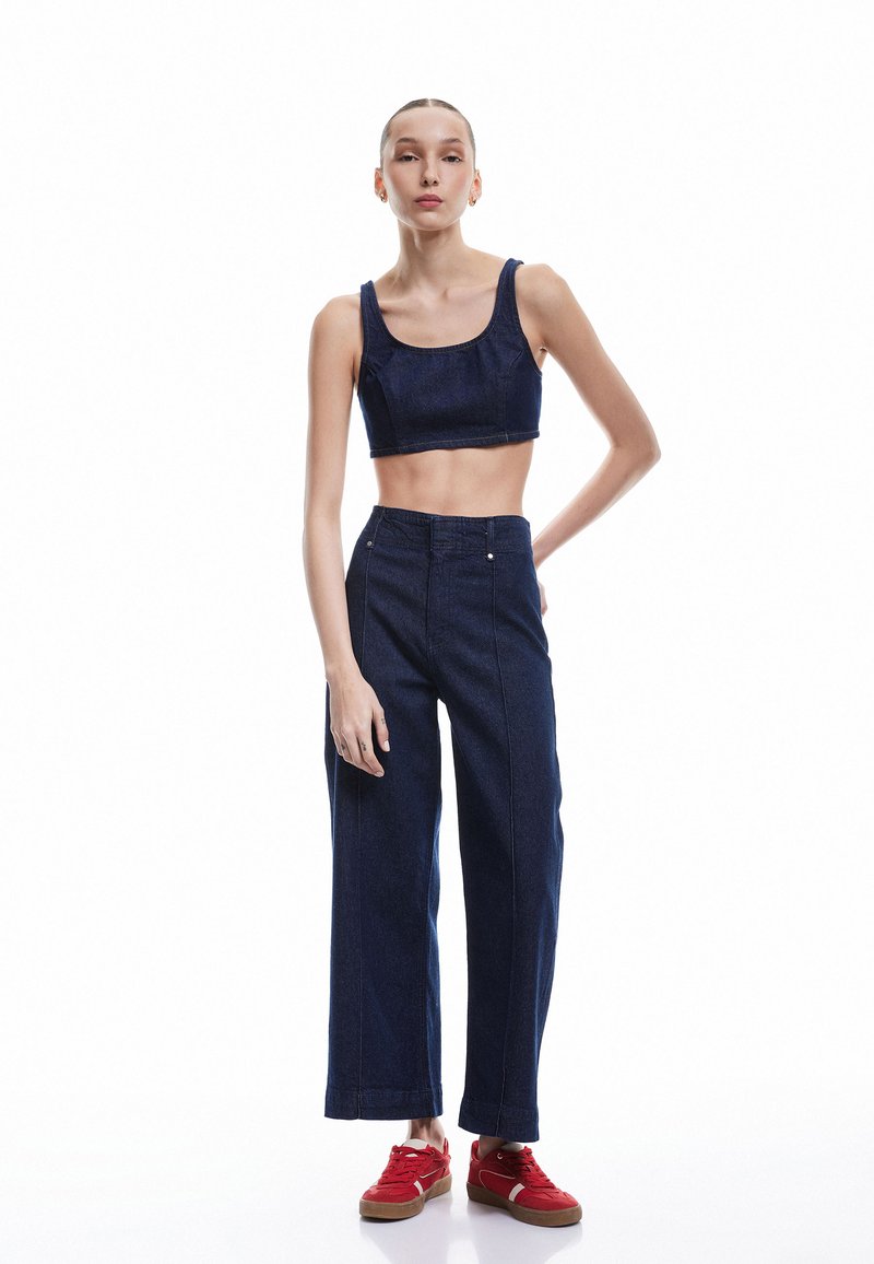 Top corto de mezclilla oscura y pantalones vaqueros de pierna ancha, con una textura suave, líneas rectas y botones de metal. Combinado con zapatillas rojas.