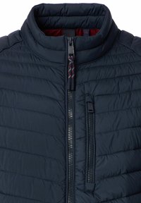 Gepolsterte marineblaue Jacke mit hohem Kragen, ausgestattet mit einem zentralen Reißverschluss und horizontalem Steppmuster. Innen ist sie rot. Strapazierfähiger Stoff.