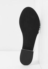 Black rubber sole with a curved shape, white heel accent, and stamped details. Smooth texture and closed design visible from the bottom view.