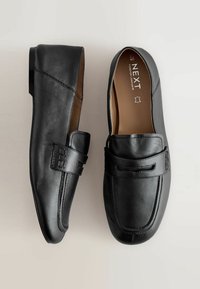 Pair of black leather loafers with moc toe stitching and strap detail, labeled size 40, on a light neutral background.