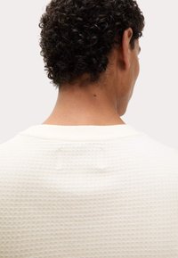 Crèmekleurig shirt van waffle-gebreid materiaal met een geribde halslijn, een textuur achterop en een subtiele patch-detail op het bovenste deel van de rug.