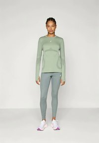 Világoszöld sport hosszúujjú póló és hozzá illő leggings, amelyek testhez simuló kialakítással rendelkeznek. Fehér sportcipő lila részletekkel teszi teljessé az öltözéket.