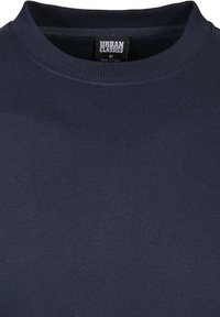 Sudadera de algodón azul marino con un cuello redondo acanalado y una textura suave. La etiqueta incluye "Urban Classics", tamaño "M" y origen "Hecho en China."