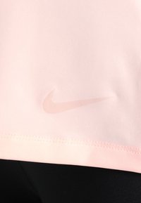 Zbliżenie na różową tkaninę z połyskującym logo Nike w kształcie znaku Swoosh wytłoczonym blisko przeszytego brzegu, ponad czarną odzieżą.