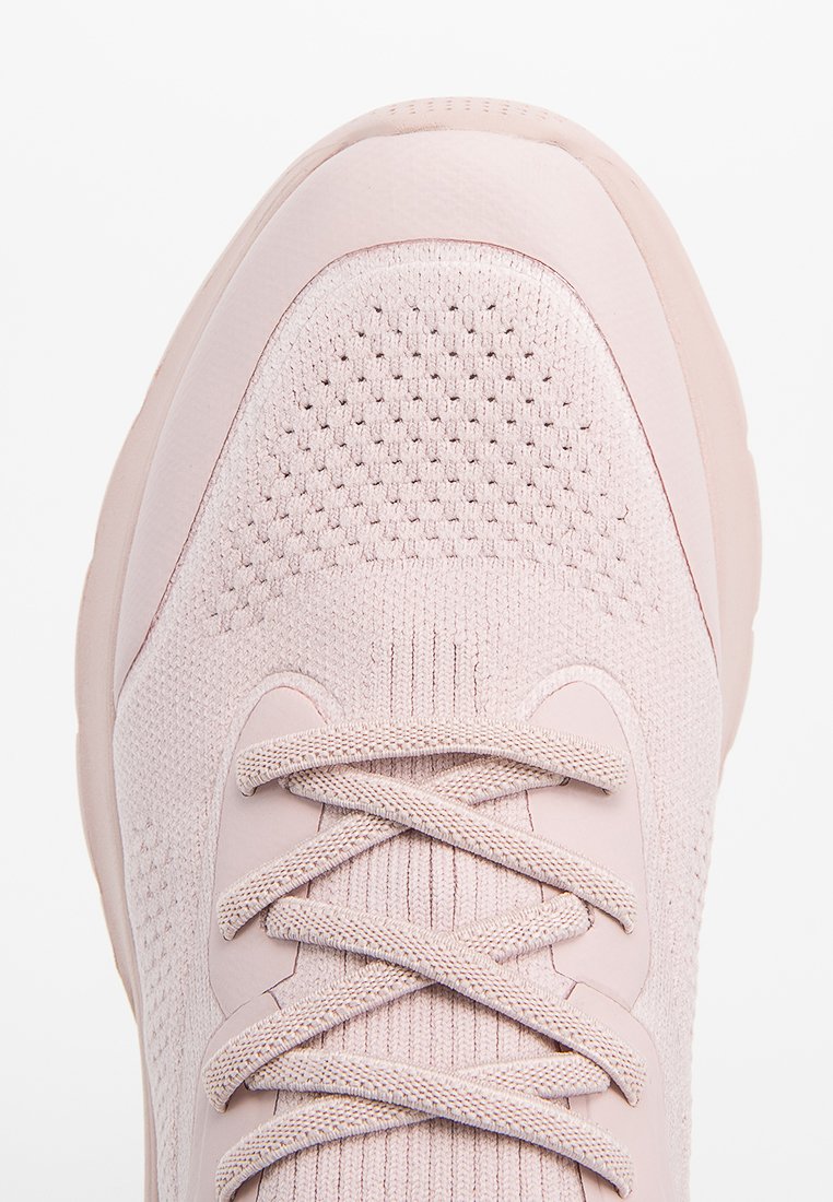 Sneaker lavorato a maglia rosa chiaro con superficie testurizzata, suola spessa e lacci incrociati, visto dall'alto su uno sfondo bianco.