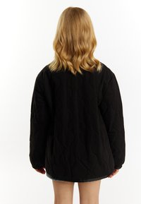 Sort quiltet jakke med et løst fit, prydet med et bølgemønster og lange ærmer. Designet er simpelt og funktionelt i stilen.