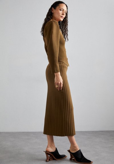 Bruine geribbelde gebreide cardigan met een aansluitende silhouet, gecombineerd met een bijpassende lange geribbelde rok. Zwarte bicolor open-toe muilen met houten hakken.