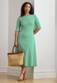 Green and white striped midi dress with three-quarter sleeves, accompanied by a tan straw tote bag with leather accents and strappy sandals.