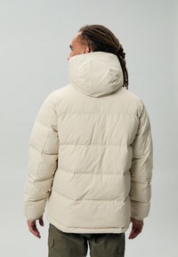 Beige gewatteerde jas met een hoge kraag en een capuchon, met een quiltpatroon en een zachte, gladde textuur, gecombineerd met olijfgroene broek.