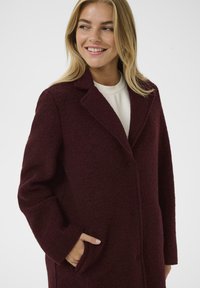 Bordo plašč iz volnene mešanice s ovratnikom, dolgimi rokavi in sprednjimi žepi; strukturirana tkanina z gumbnimi zaponkami. Enostaven, sodoben dizajn.