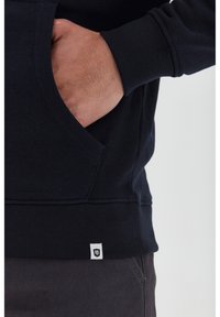Sudadera navy con puños y dobladillo de canalé, que cuenta con un bolsillo frontal. Una pequeña etiqueta de marca blanca es visible en la parte inferior izquierda.