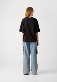 Black cotton t-shirt with short sleeves, paired with wide-leg blue denim cargo pants featuring side pockets and a textured fabric.
