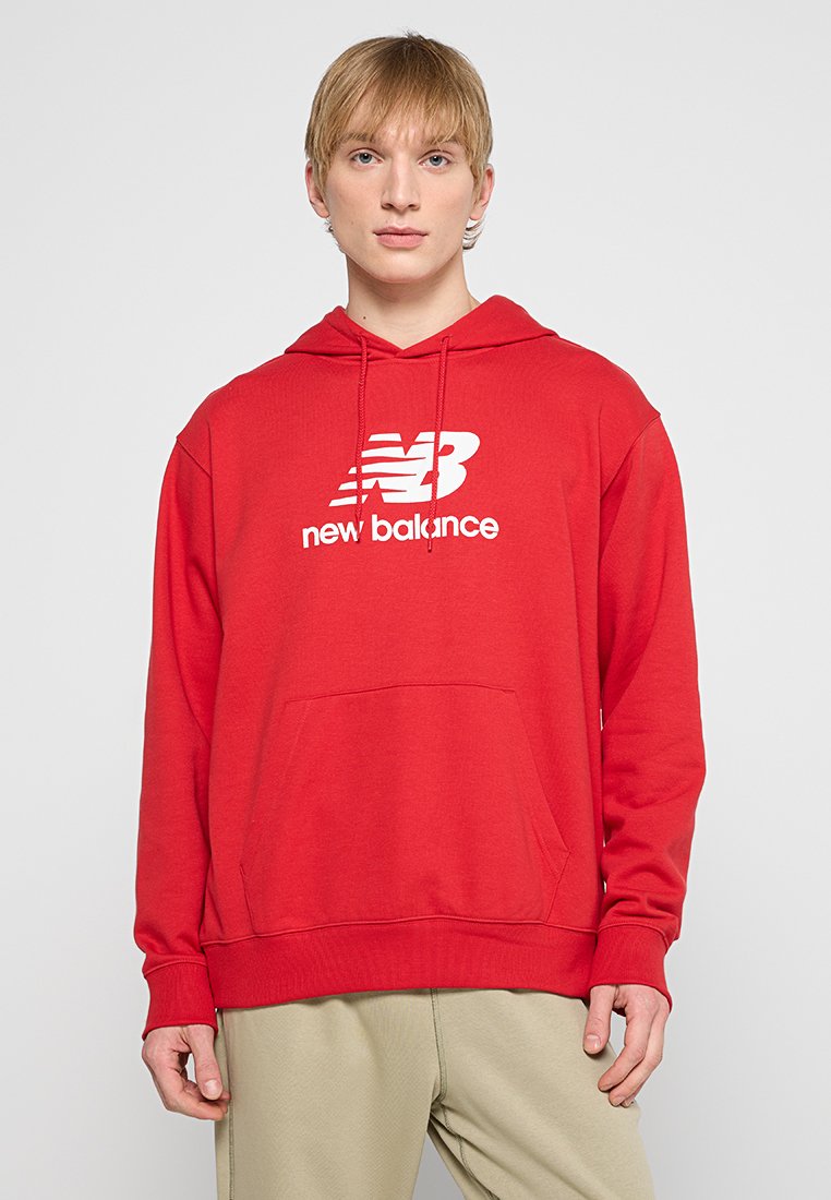 Sweat à capuche rouge en mélange de coton, avec une poche kangourou à l'avant, des poignets côtelés et un logo "New Balance" blanc. Texture lisse.