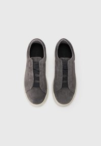 Par de zapatillas de ante gris sin cordones con bandas elásticas negras en la parte superior y suelas de goma blanca sobre un fondo blanco.