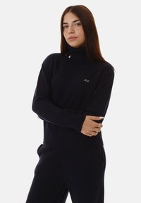 Maglione a collo alto blu navy con texture a coste, caratterizzato da un piccolo logo sul petto. Maniche lunghe e design aderente. Materiale in maglia morbida.