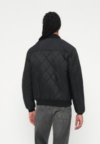 Sort quilted bomberjakke med diamantmønster, ribbede manchetter og kant. Har en glat overflade og en afslappet pasform. Kun bagansigt.