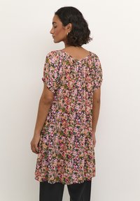 Blomstret tunika-kjole med korte �ærmer, prydet med et farverigt mønster af pink, lilla og grønne blomster på en sort baggrund. Blødt stof.