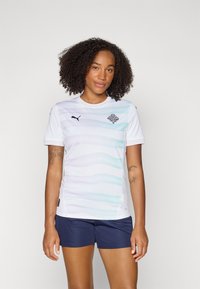 White sports jersey with subtle wavy light blue patterns, black logo on chest. Paired with dark blue shorts, made from breathable fabric.