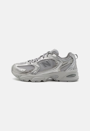 Sølv og grå atletiksneaker med meshstof, snørelukning foran, polstret sål og mærkevare detaljer på siden og hælen.