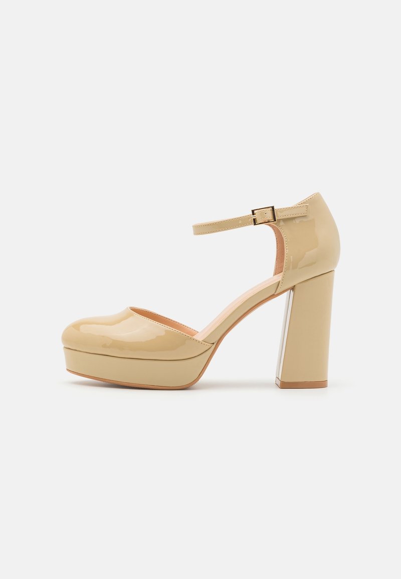 Chaussure à plateforme en cuir verni beige avec bride à la cheville et talon bloc sur fond blanc.