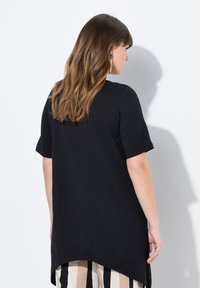 Top negro de manga corta con dobladillo redondeado, hecho de una tela ligera, que presenta un ajuste relajado y una textura suave. Diseño minimalista.