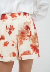 Bloemige shorts van een lichte stof met een crème basis en grote rode en oranje bloemenprints. Aansluitende taille met zijplooien en omgerolde zomen.