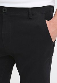 Zwarte katoenen broek met een rechte pasvorm, voorzakken en een enkele knoopsluiting bij de tailleband. Glad oppervlak.