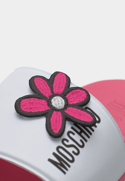 Sandale blanche à glissière avec le texte "Moschino" en noir et une décoration de fleur rose brodée sur la bride au-dessus d'une semelle rose.