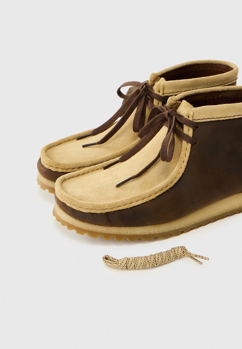 Chaussures en cuir marron et en suède beige avec une pointe ronde, un dessus contrastant et des lacets marron. Comprend un lacet beige à motifs laissé à proximité.
