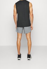 Svart ärmlös topp, grå sportshorts och svarta löparskor. Shortsen har vita accenter. Slät tyg, figursydd design.