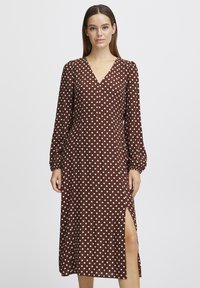 Robe marron à pois avec de longues manches bouffantes, un décolleté en V et une fente haute jusqu'à la cuisse. Fabriquée en tissu lisse avec une drapé élégant.