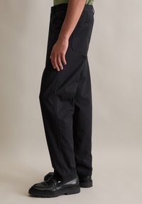 Zwarte katoenen broek met een recht model, zijzakken en een eenvoudig ontwerp, gecombineerd met zwarte leren schoenen.