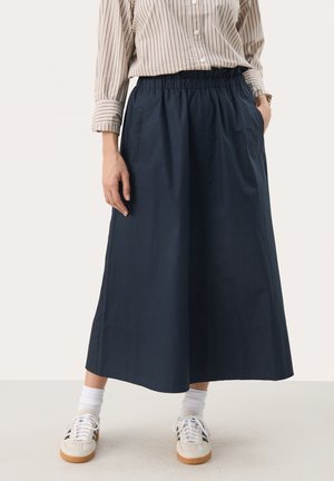 Jupe midi en coton bleu marine avec une taille élastique, des poches latérales et une texture lisse, associée à des baskets blanches et des chaussettes montantes.