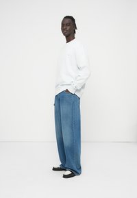 Ανοιχτό μπλε φούτερ με μακριά μανίκια, συνδυασμένο με μπλε τζιν παντελόνι σε υπερμεγέθη γραμμή. Μαύρα και λευκά αθλητικά παπούτσια ολοκληρώνουν την εμφάνιση. Απλός σχεδιασμός, χωρίς σχέδια.