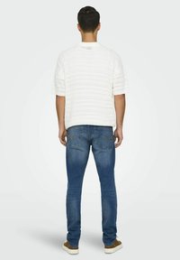 Top de punto blanco de manga corta con un patrón texturizado, combinado con unos vaqueros de denim azul. Las zapatillas son marrones con suelas blancas.