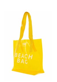 Keltainen läpinäkyvä rannalaukku, jossa valkoinen teksti "BEACH BAG." Ominaisuuksiin kuuluu tukevat keltaiset kangasnyörit ja avoin yläosa.