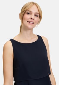 Námořnická bezrukávová blůza s kulatým výstřihem, vrstveným designem a jemnou tkaninou. Disponuje decentní kapsičkou, hladkou strukturou a elegantním splýváním.
