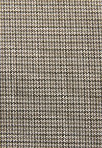 Tissu tissé avec un petit motif à carreaux en nuances de brun, beige et blanc ; surface texturée avec un mélange de fils foncés et clairs.