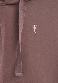 Sudadera color burdeos hecha de tejido texturizado que presenta un logo de golfista bordado en blanco y un cordón regulador. Incluye una discreta etiqueta con el logo en el dobladillo.