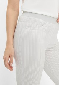 Hellgraue gestreifte Hose mit einem dehnbaren Bund und zwei Gesäßtaschen, die kleine Knöpfe und eine weiche Textur aufweist.