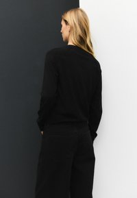 Zwart longsleeve shirt met een relaxed fit, ronde halslijn en raglanmouwen; gecombineerd met zwarte denimbroek met achterzakken.