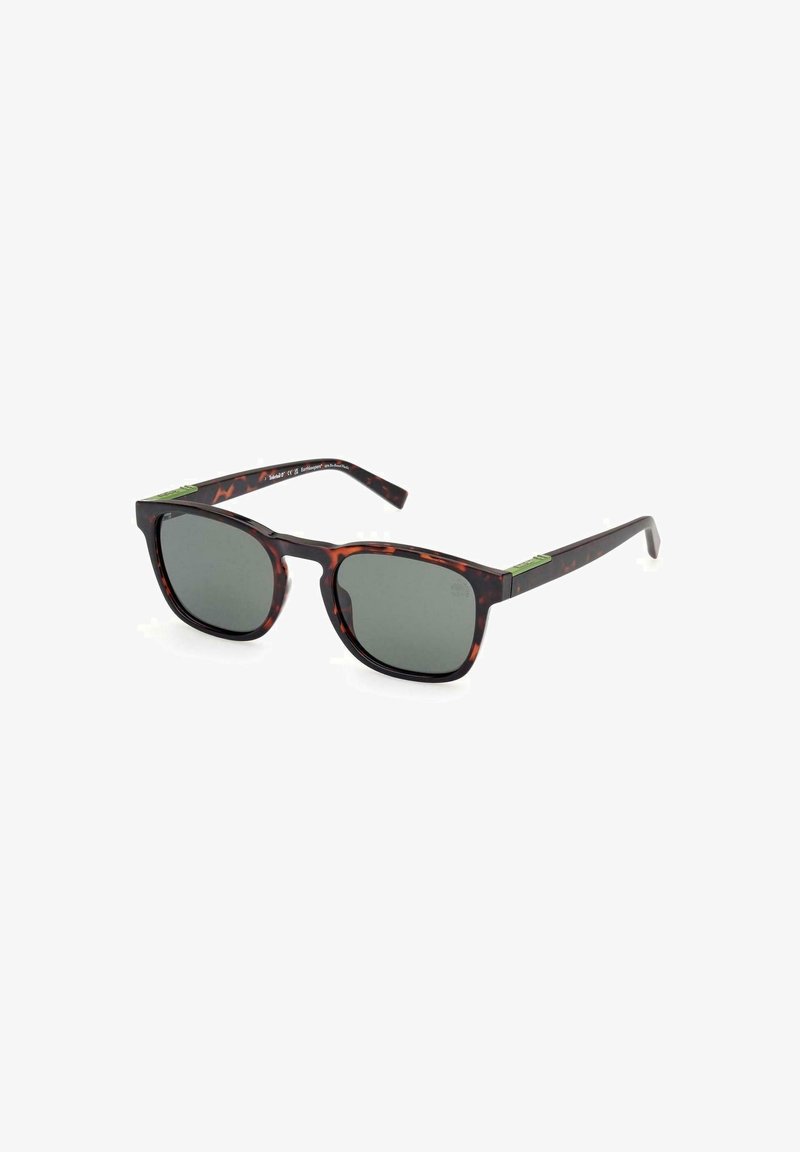 Gafas de sol de carey con lentes oscuros, forma rectangular, montura gruesa, acento verde en la patilla y brazos negros delgados.