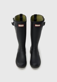 Μαύρα λαστιχένια μπότες σε ύψος μέχρι τον αστράγαλο με πράσινη επένδυση, λεπτομέρεια με λουράκι στο πλάι και λογότυπο στο μπροστινό μέρος. Λείο υλικό και στρογγυλεμένος σχεδιασμός μύτης.