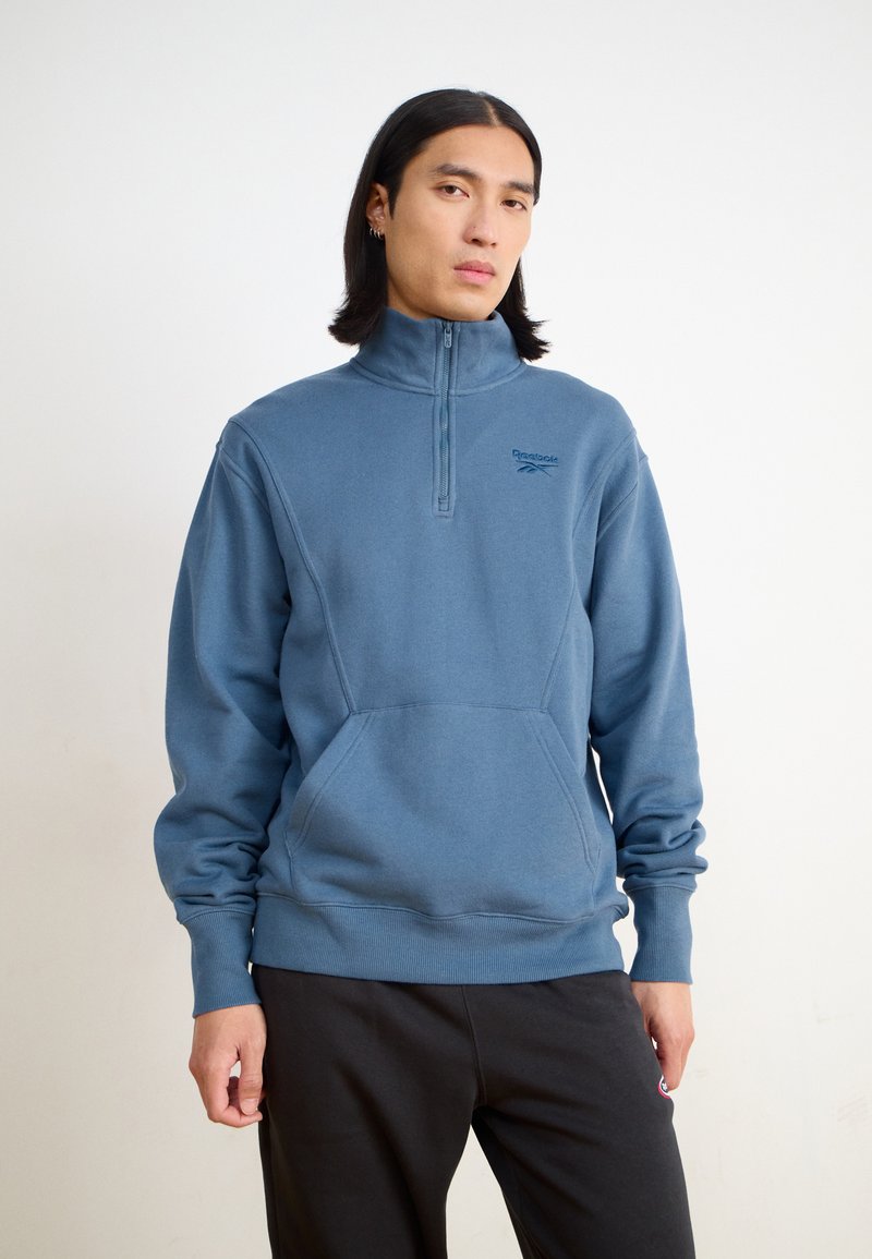 Felpa in pile azzurro chiaro con colletto alto e tasca frontale. Presenta una chiusura con mezza zip e polsini e orlo a costine.