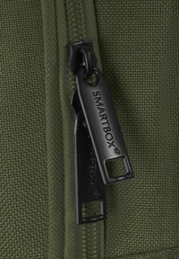 Gros plan sur deux tirettes de fermeture éclair SMARTBOX noires sur un tissu vert tissé avec des dents de fermeture éclair visibles.
