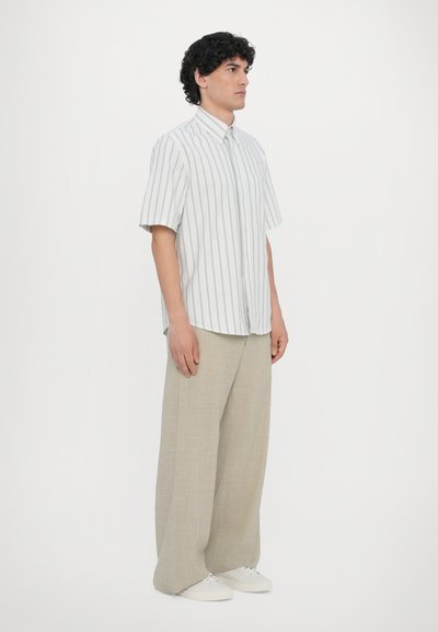 Kortermet, knappet skjorte i hvit med grå vertikale striper, kombinert med beige vide bukser og hvite sneakers.