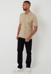 Camisa de botones de manga corta en color beige con patrones de diamante texturizados, combinada con pantalones negros y zapatillas blancas. Diseño minimalista, color sólido.