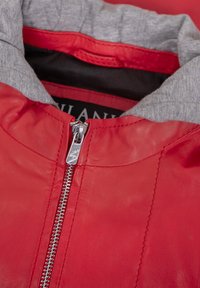 Rote Lederjacke mit einem grauen Stofffutter, silbernem Reißverschluss und einem runden Kragen. Die Jacke hat eine glatte Textur und gestickte Details.