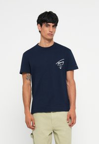 Marineblå bomulds T-shirt med korte ærmer, rund halsudskæring og hvid tekstlogo på venstre bryst. Glat tekstur, klassisk fit design.